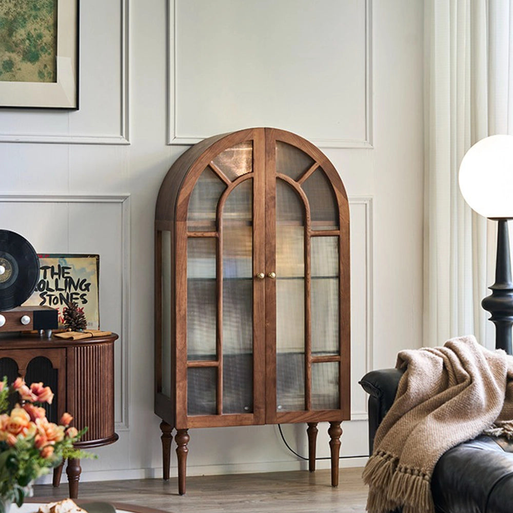 Brown arched display cabinet with patterned glass double doors and turned legs in a living room.