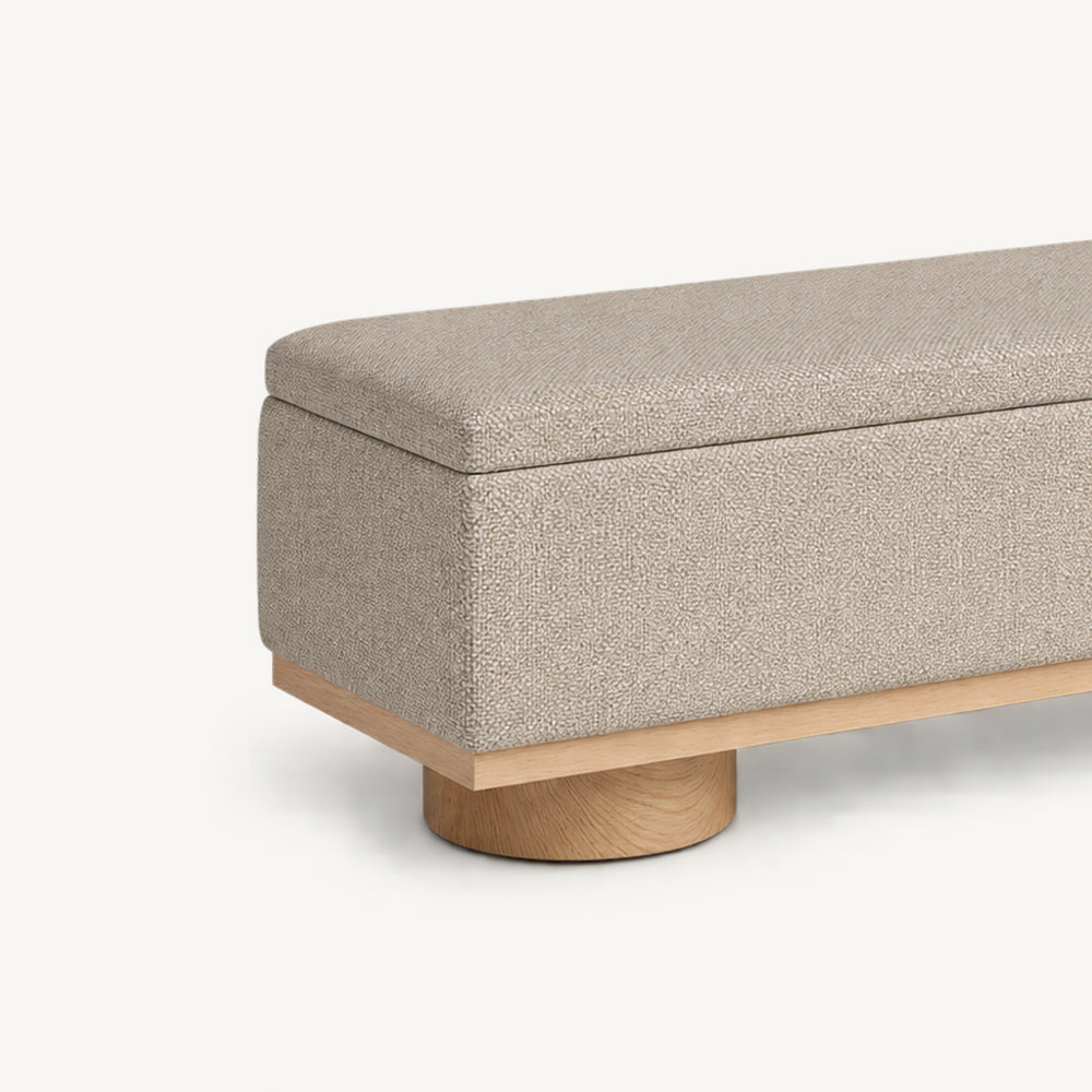 Close-up of the beige bench's padded lid corner, upholstered side and cylindrical foot.