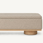 Front detail of the beige bench's lid seam, textured upholstery and wood-tone base trim.