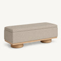 Beige upholstered bench with a padded rectangular lid, narrow light wood-tone base and round feet.