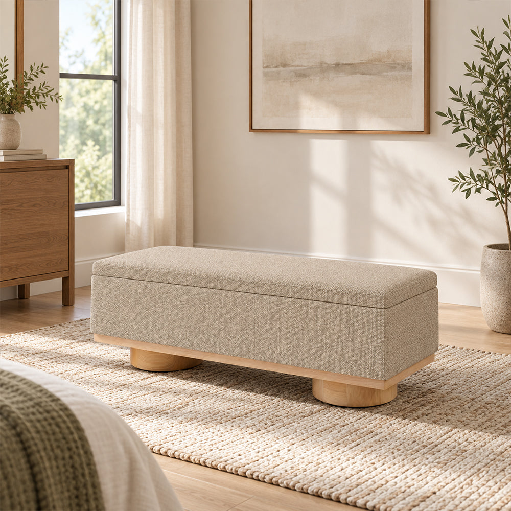 Beige upholstered storage bench with a rectangular padded top and short round wood-tone feet.