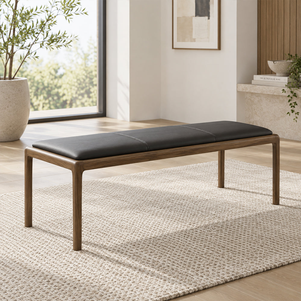 Black upholstered bench with a brown frame and slim legs, shown beside a window.