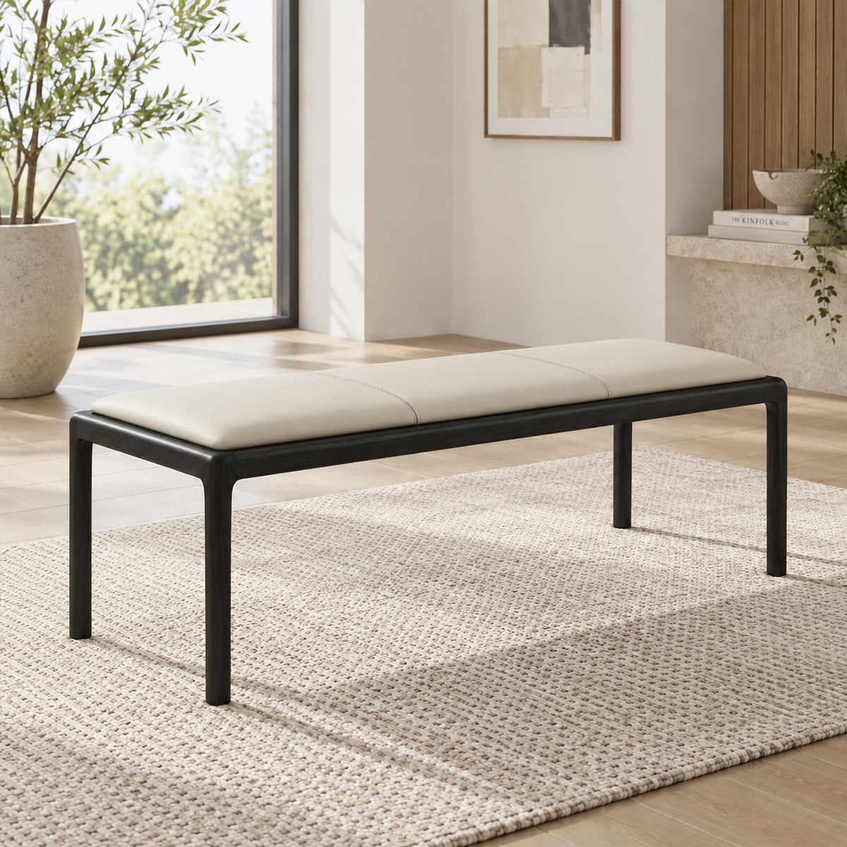 Cream upholstered bench with a dark frame and slim legs beside a window.