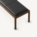 Overhead detail of the bench's black stitched cushion above a rounded wood-tone frame corner.