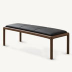 Bench with a black cushion divided by stitched seams, supported by a slim rounded brown frame.