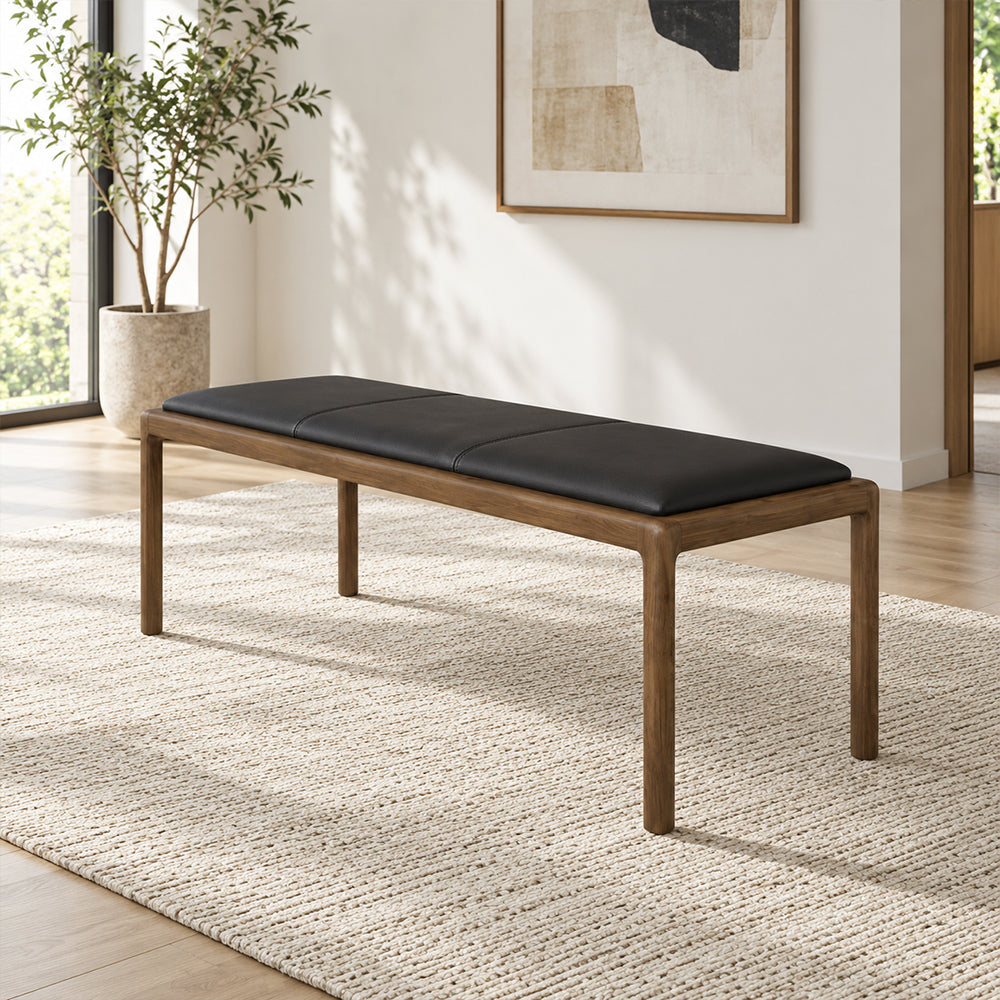Black upholstered bench with a thin wood-tone frame and slender legs in a sunlit room.