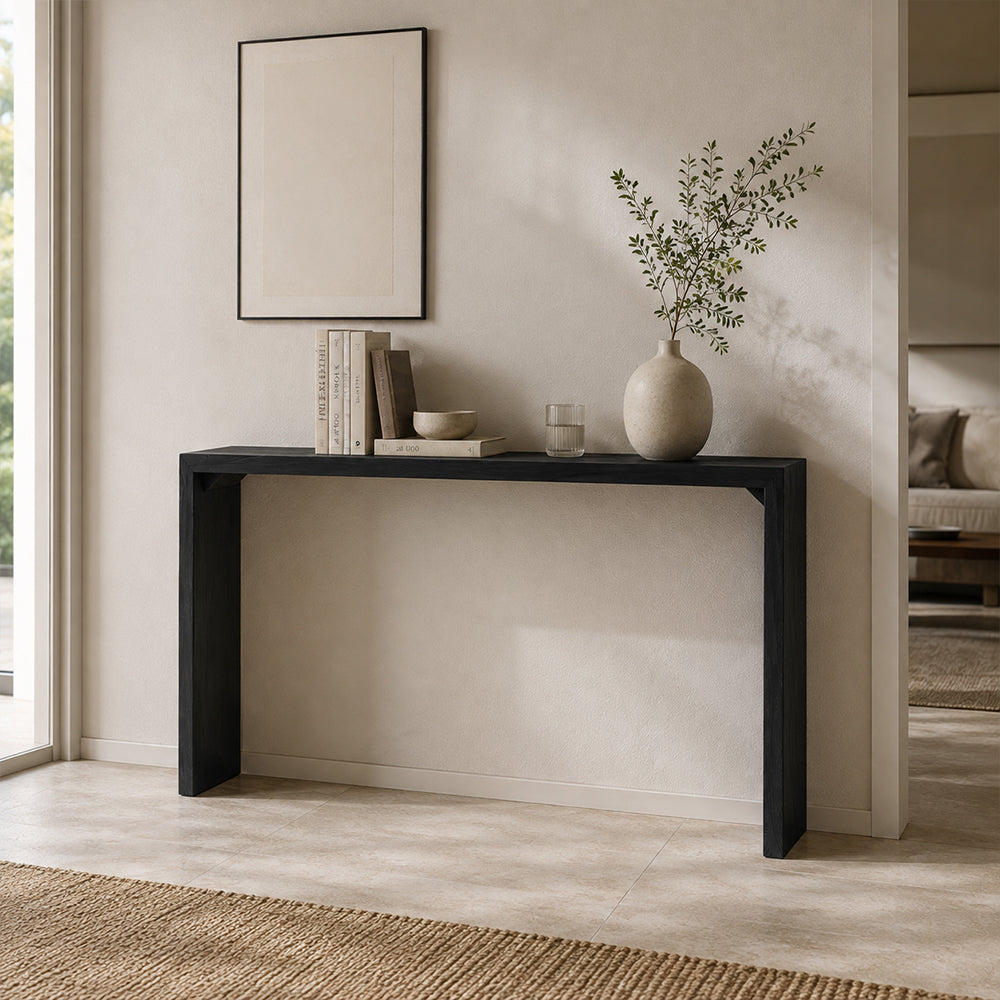 Black narrow console table with slab sides, styled with a vase and books beneath artwork.