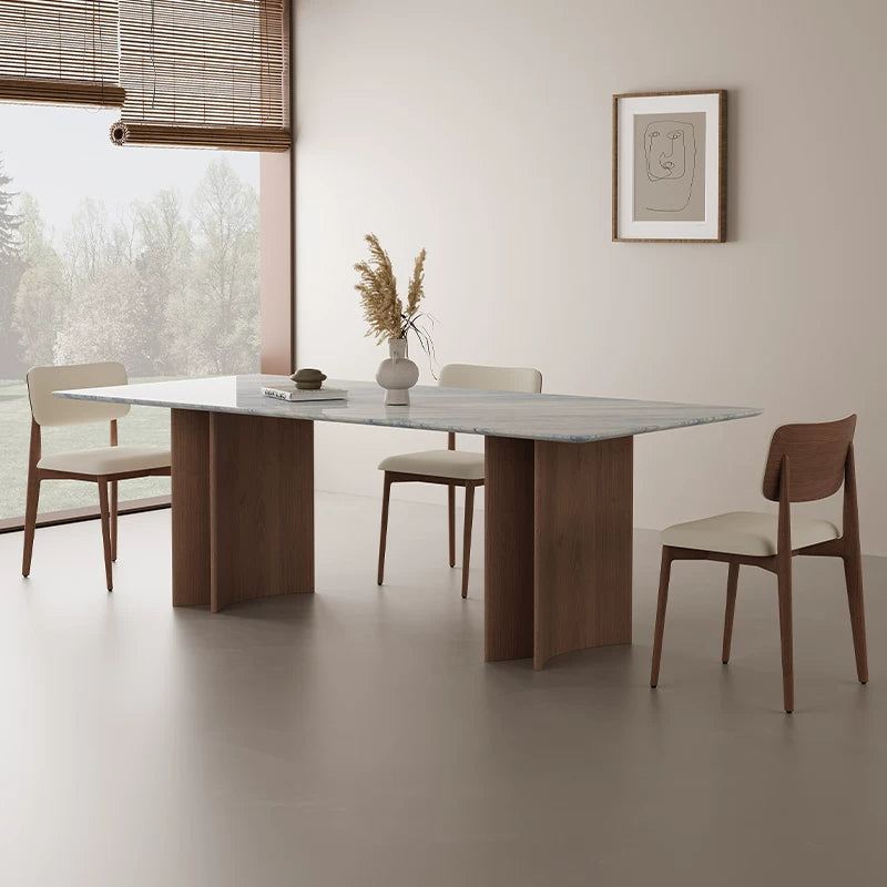 Blue-gray veined dining table with curved wood-tone bases beside a window in a neutral dining room.