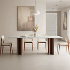 Rectangular dining table with a blue-gray veined top and two brown panel bases, surrounded by cream upholstered chairs.
