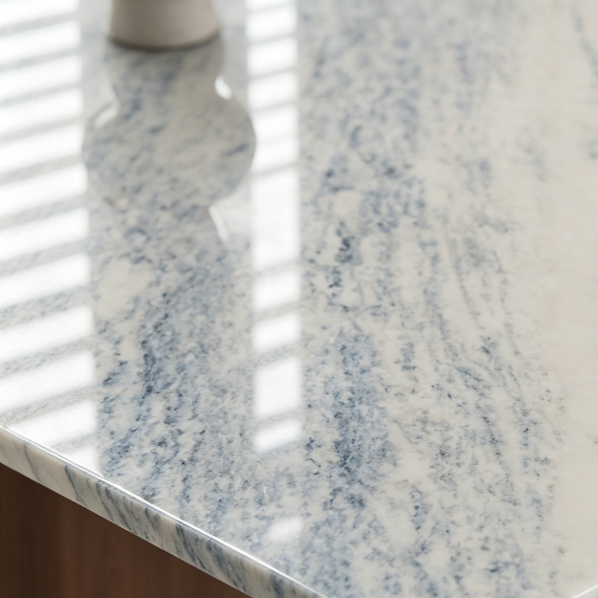 Close-up of the pale dining tabletop with flowing blue-gray veining and light reflected across its surface.