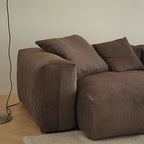 Close-up of the brown sofa's rounded broad arm and textured accent pillows.