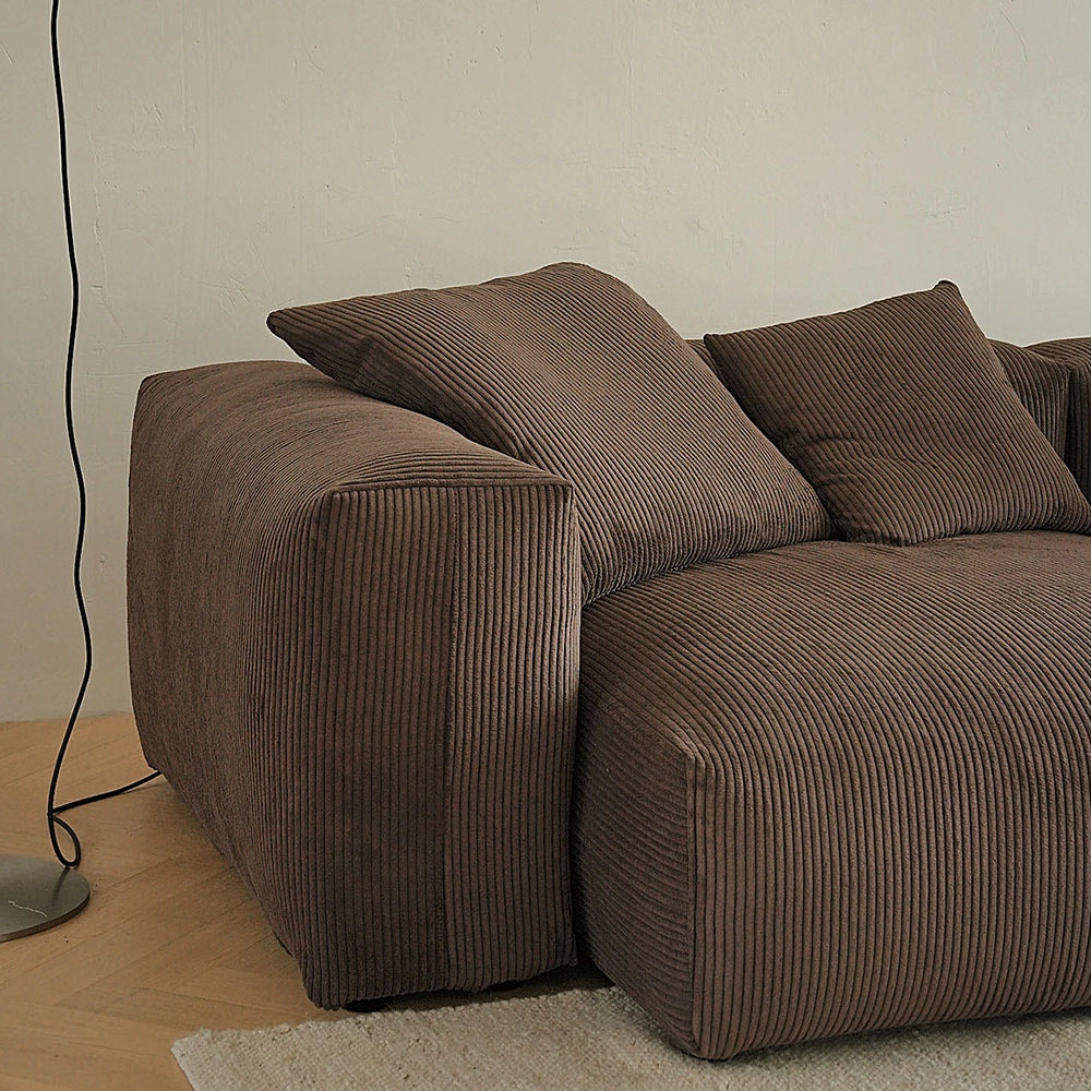 Close-up of the brown sofa's rounded broad arm and textured accent pillows.