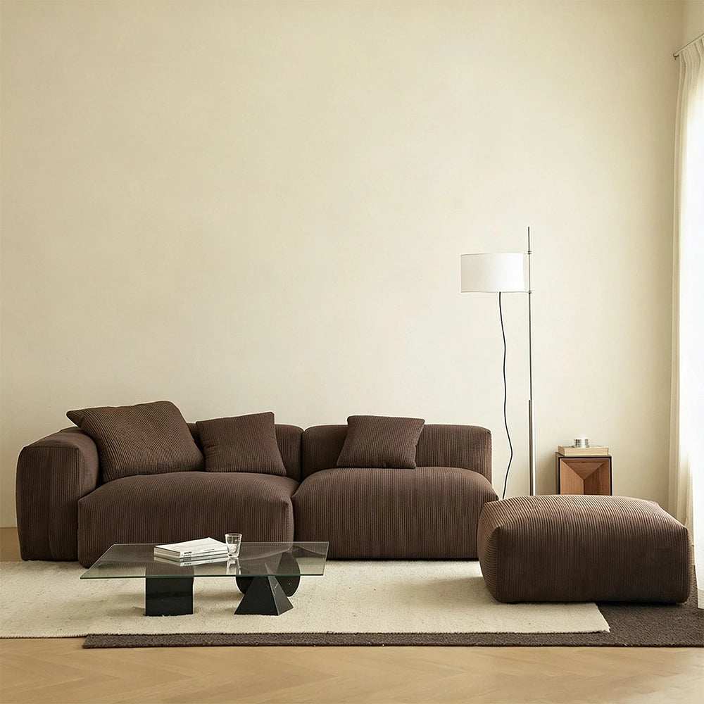 Brown ribbed-upholstery modular sofa with loose cushions and a separate ottoman on a pale rug.