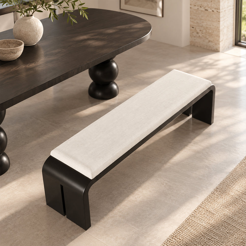 Cream-cushioned bench with a curved black frame beside a dark dining table, viewed from above.