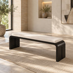 Black slab-frame bench with a long cream cushion on a rug in a sunlit room.