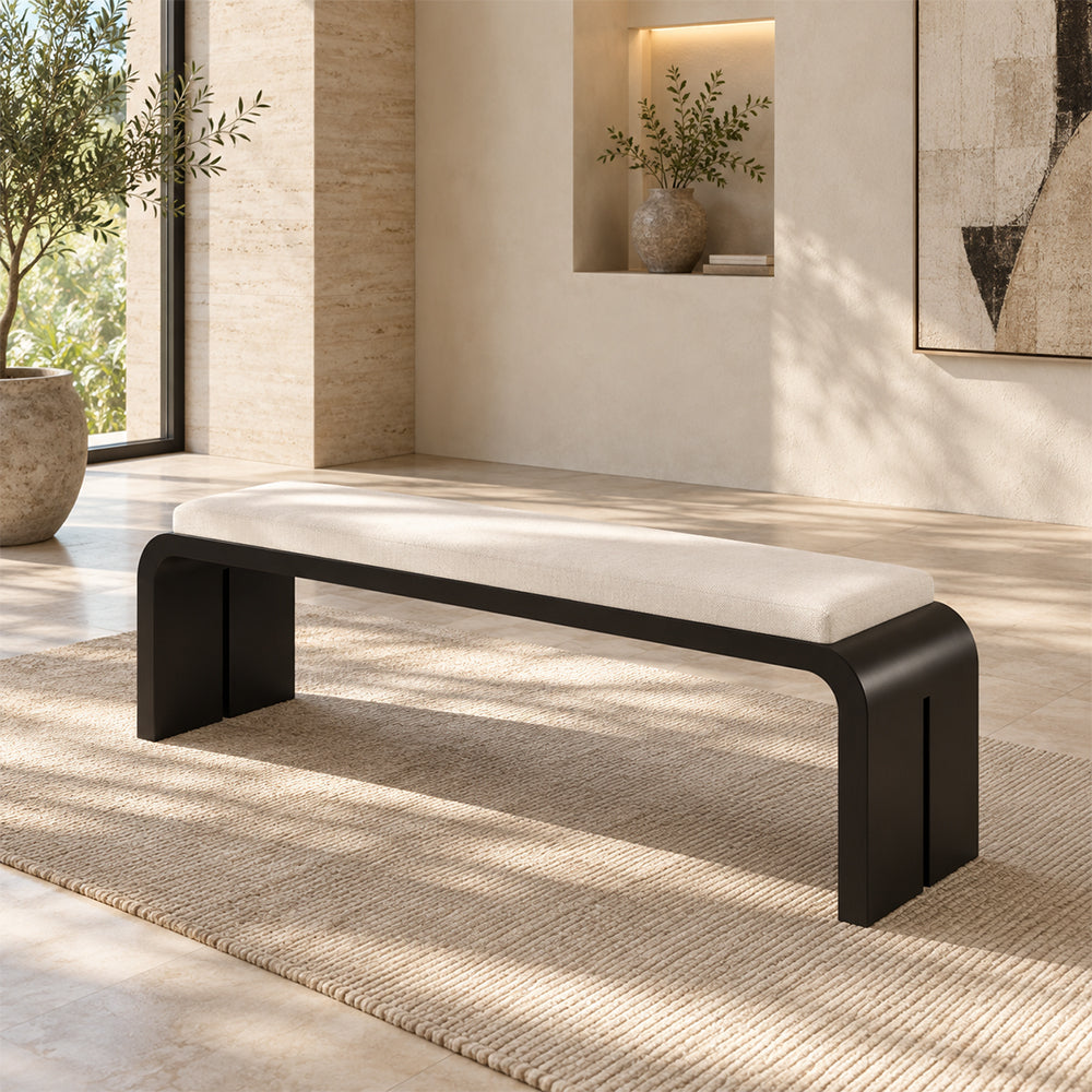 Black slab-frame bench with a long cream cushion on a rug in a sunlit room.