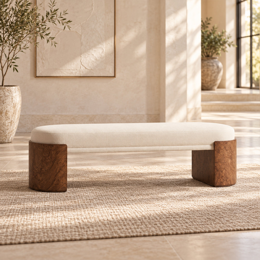 Cream cushioned bench with rounded brown end supports and a slim upholstered crossbar in a sunlit room.