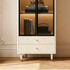 Close-up of the cream cabinet's lower glass shelf, two fluted drawers and raised feet.