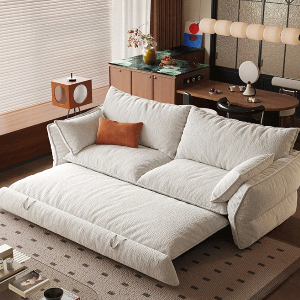 Cream sofa bed with its pull-out sleeping section extended beneath loose back cushions and padded arms.