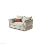 Compact cream sofa bed with two loose back cushions, padded arms and an orange accent pillow.