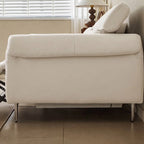 Side profile of the cream reclining sofa showing its padded arm, raised back and slim legs.