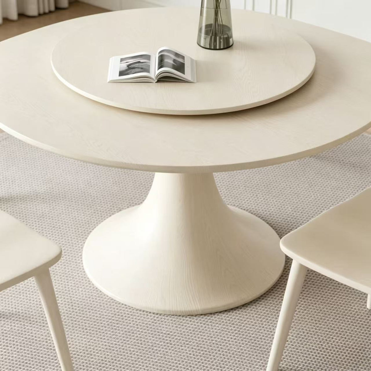 Close-up of the cream dining table's rounded top, raised turntable and flared pedestal.