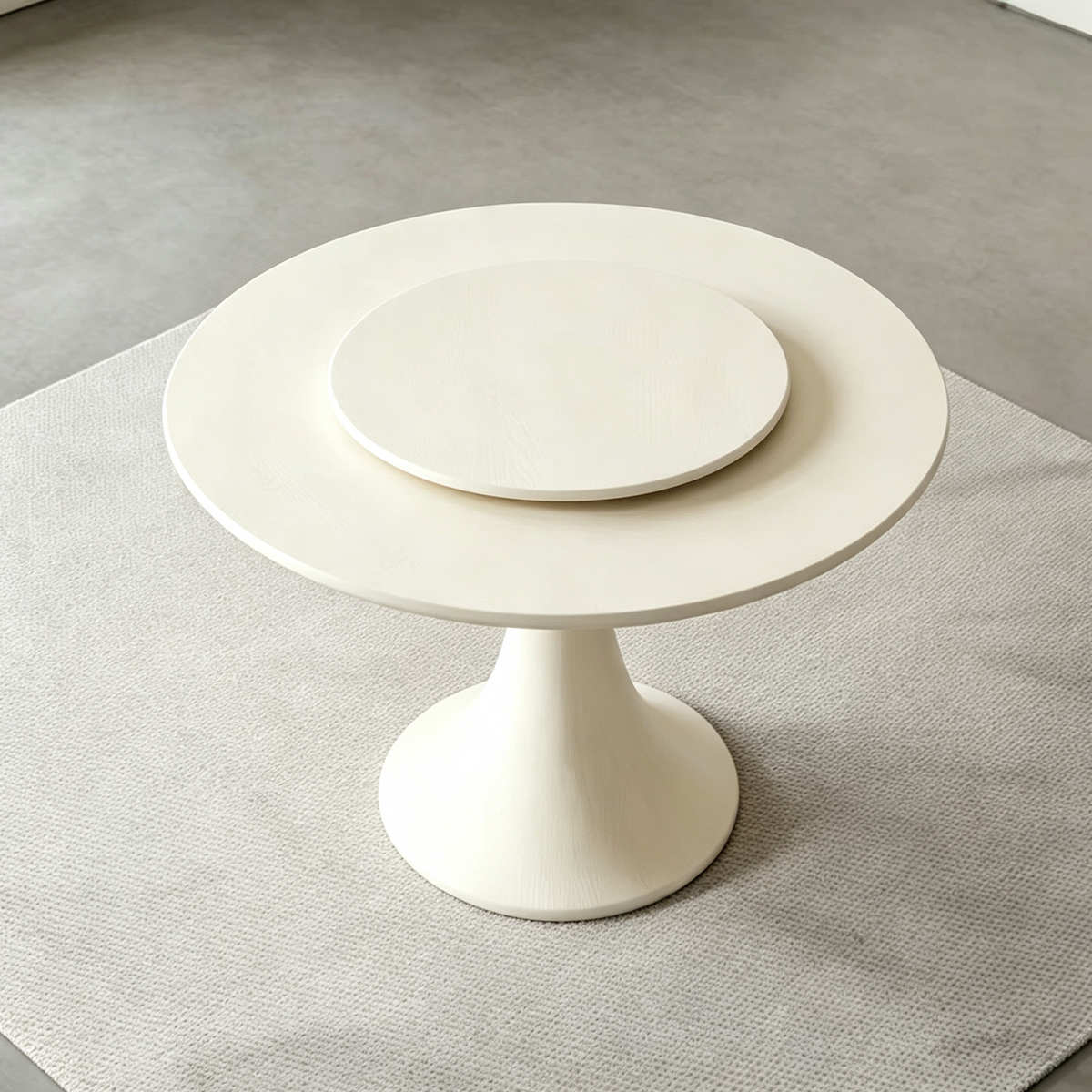 Cream circular dining table with a matching raised turntable and flared central pedestal.