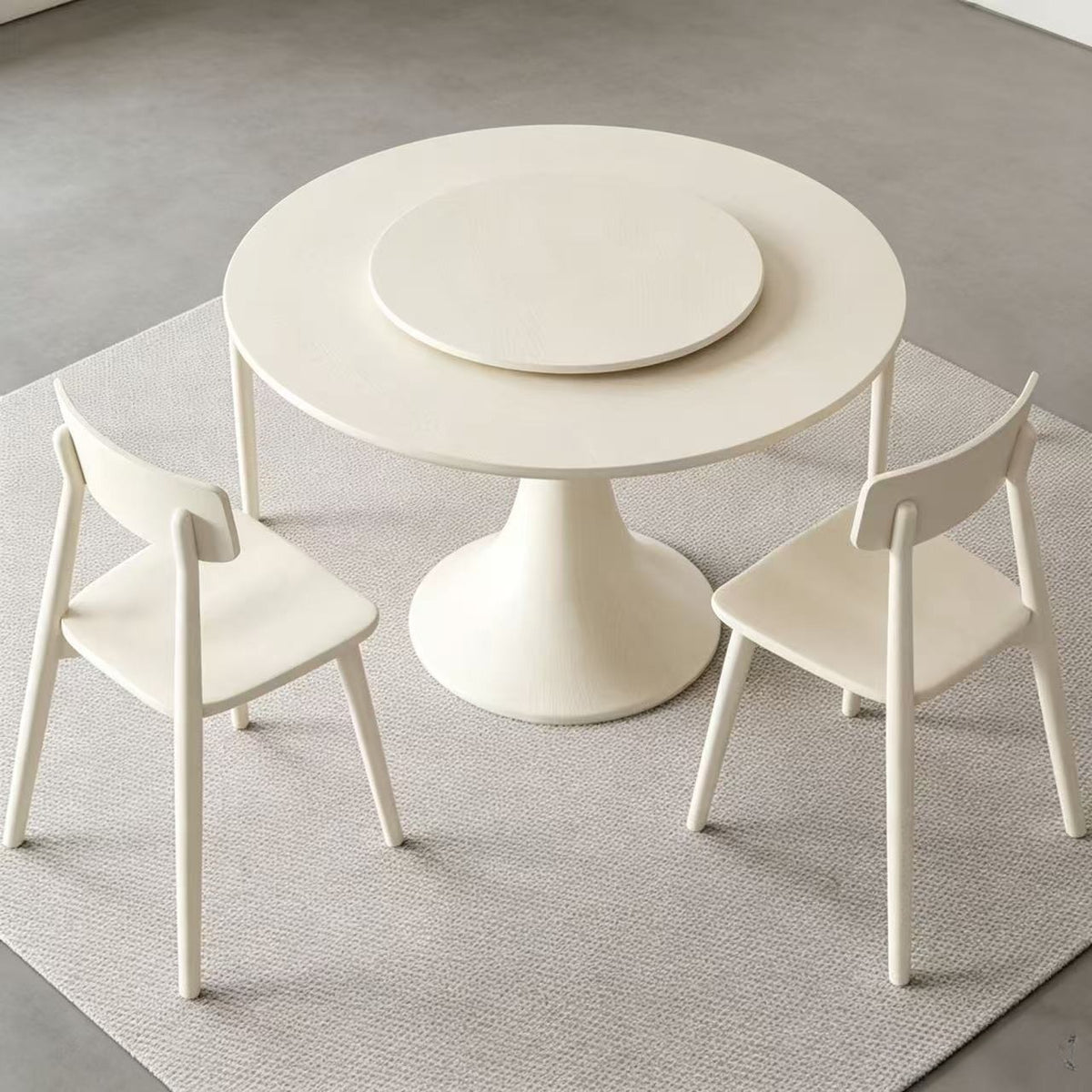 Cream round pedestal dining table with an empty central turntable and pale chairs around it.