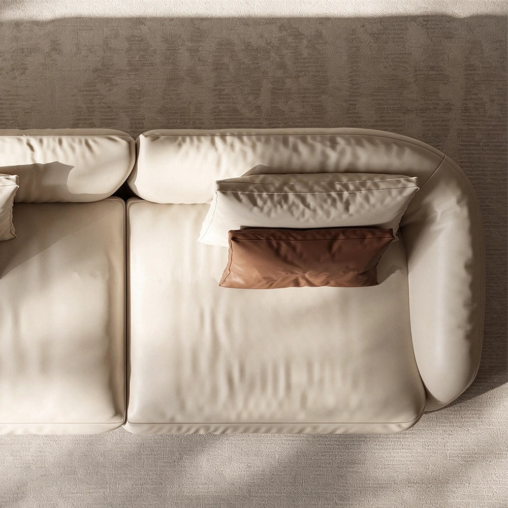 Overhead detail of a cream sofa end module with a rounded arm and stacked accent cushions.