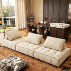 Cream armless modular sofa with deep tufted seats in a living room beside a dining area.