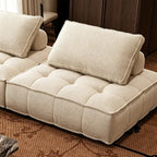 Detail of a cream tufted sofa module, showing its piped edges and loose back cushion.