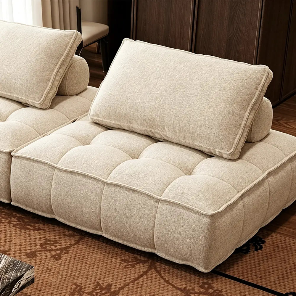 Detail of a cream tufted sofa module, showing its piped edges and loose back cushion.