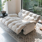 Cream loveseat with both backrests lowered and footrests extended beside a large window.