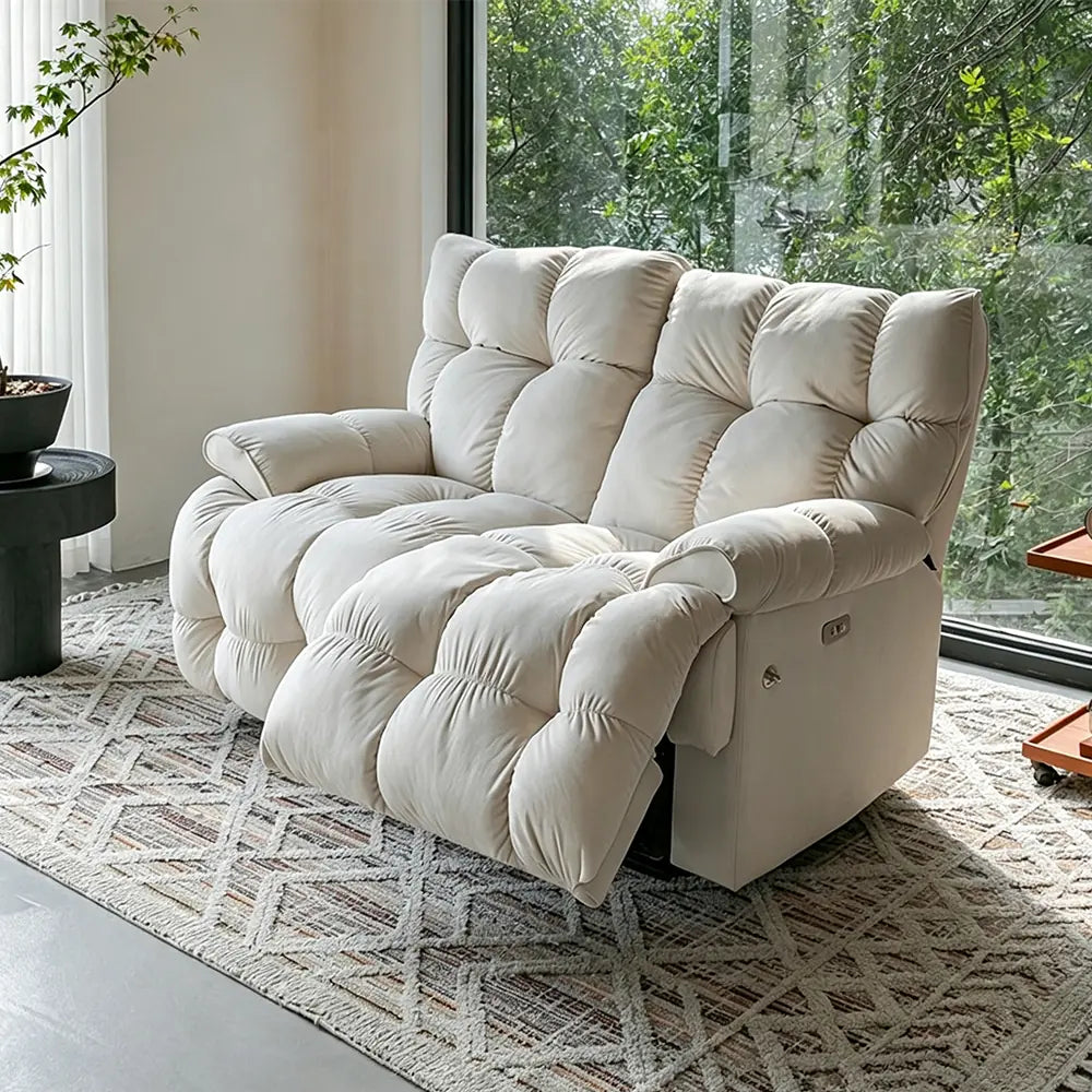 Cream deeply cushioned reclining loveseat in upright form on a patterned rug.
