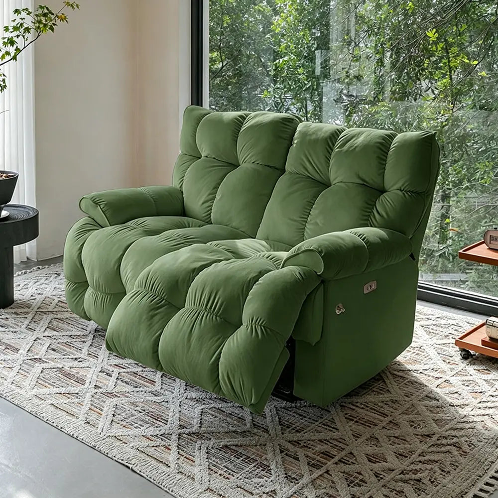 Green deeply cushioned reclining loveseat in upright form beside garden-facing windows.