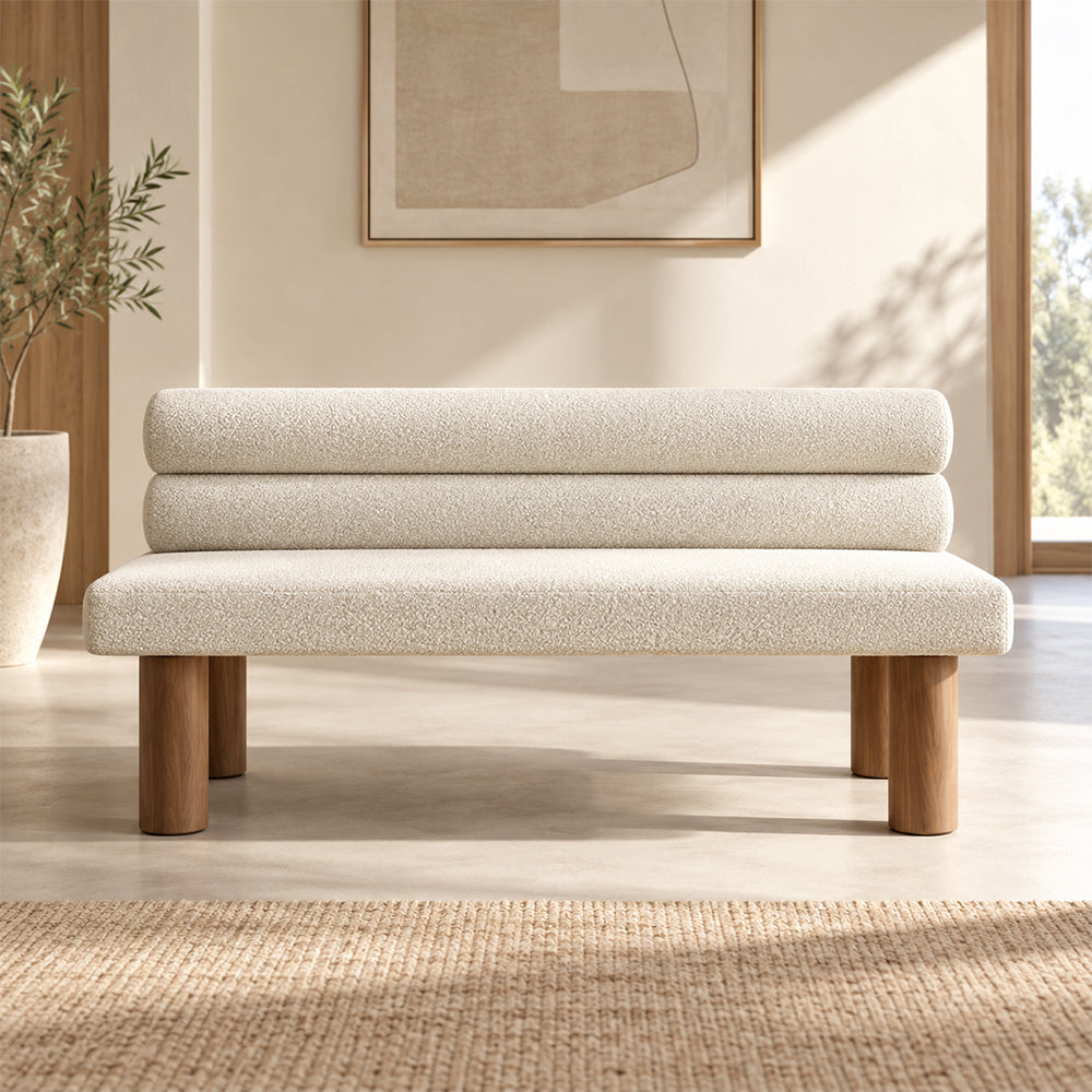 Front view of the cream upholstered bench with a double-roll backrest and cylindrical wood-tone legs.