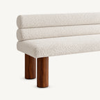 Close-up of the bench's cream textured upholstery, double-roll back and two brown cylindrical legs.