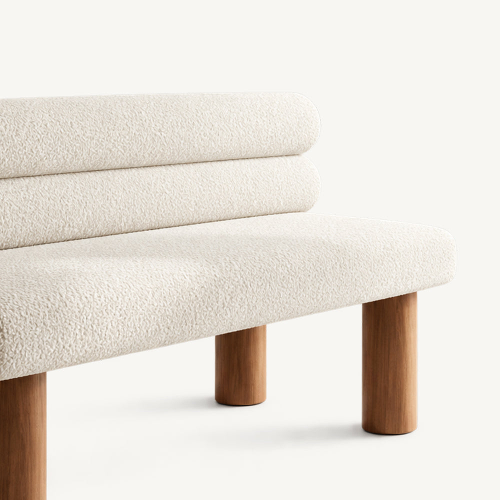 Angled detail of the cream bench's rounded seat, cylindrical back cushions and wood-tone legs.