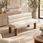 Cream textured bench with two cylindrical back cushions and brown round legs in a bright living room.