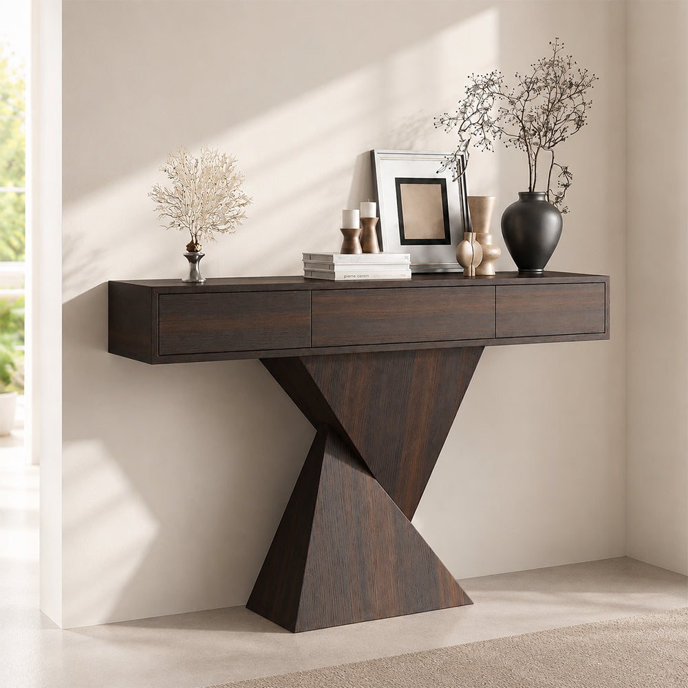Dark brown console table with three drawers and an intersecting triangular pedestal, styled with vases and frames.