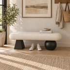 Front view of the cream bench with mismatched black geometric supports and shoes beneath the seat.
