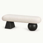 Cream rounded upholstered bench with a black tapered block leg and a black spherical leg.