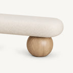Close-up of the cream bench's rounded upholstered end and light wood-tone spherical support.