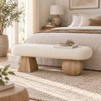 Cream upholstered bench with light wood-tone geometric supports at the foot of a bed.