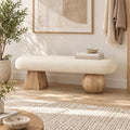 Cream upholstered bench on one light wood-tone tapered support and one light wood-tone ball-shaped support in an entryway.