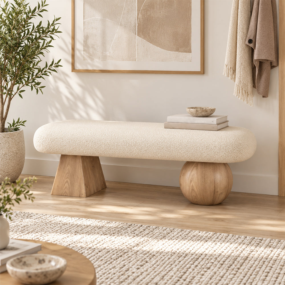 Cream upholstered bench on one light wood-tone tapered support and one light wood-tone ball-shaped support in an entryway.