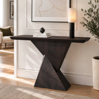 Dark brown console table with interlocking triangular pedestal panels, styled with books and a lamp.