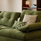 Close-up of the green sofa's angled padded arm, tufted back and patterned accent cushions.