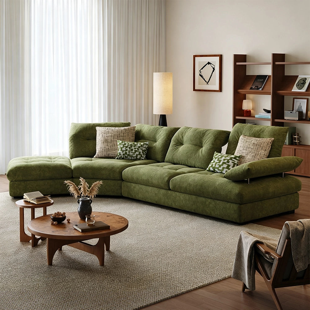Green sectional sofa with a chaise-like end and raised angled arm cushion beside wooden coffee tables.
