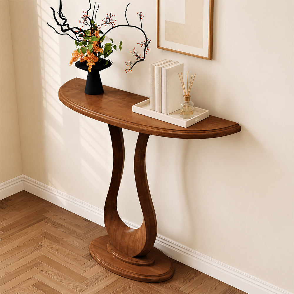 Brown half-moon console table with an open loop pedestal, styled with flowers and books.